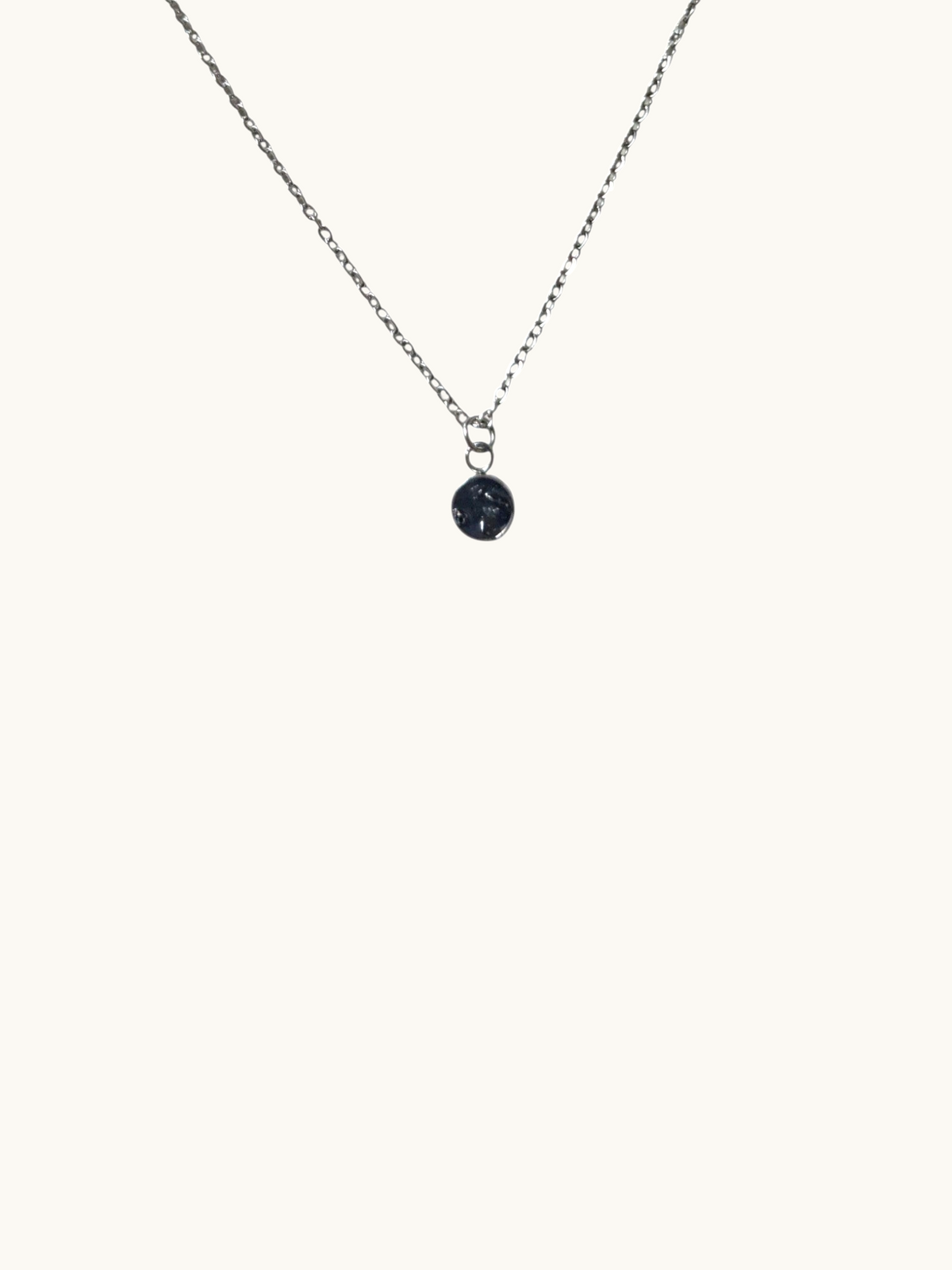 Citrinmagi silverfärgat halsband med en minimalistisk rund berlock och mörk glittrande detalj på ljus yta.