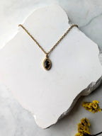 Citrinmagi handgjort halsband med oval svart obsidian infattad i 18K guldpläterat rostfritt stål på vit stenplatta