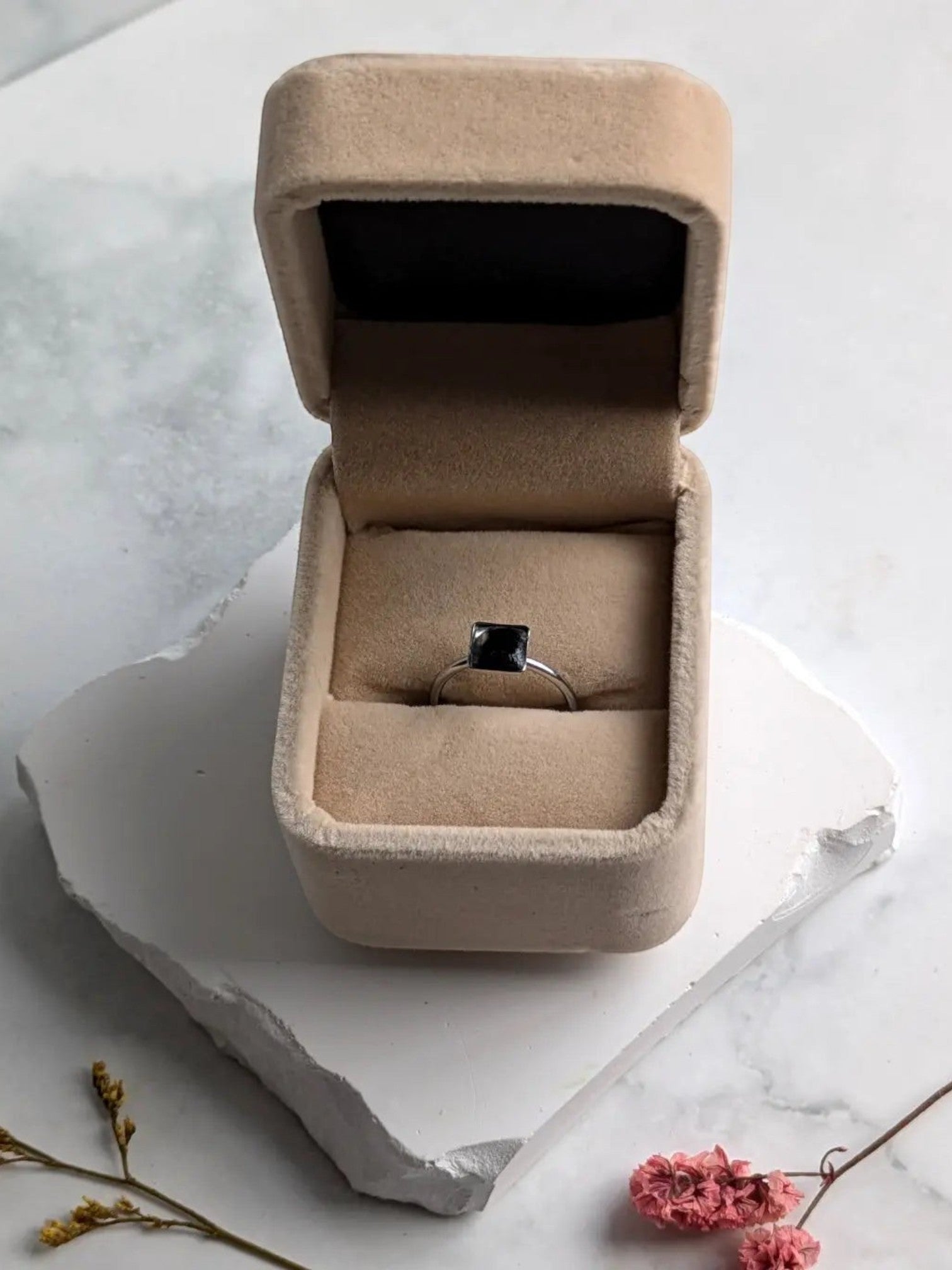 Citrinmagi fyrkantig ring i silver med svart obsidian i en beige smyckesask på en vit stenplatta.