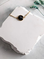 Citrinmagi armband med rund svart turmalin i 18k guldpläterad fattning på en vit stenplatta.