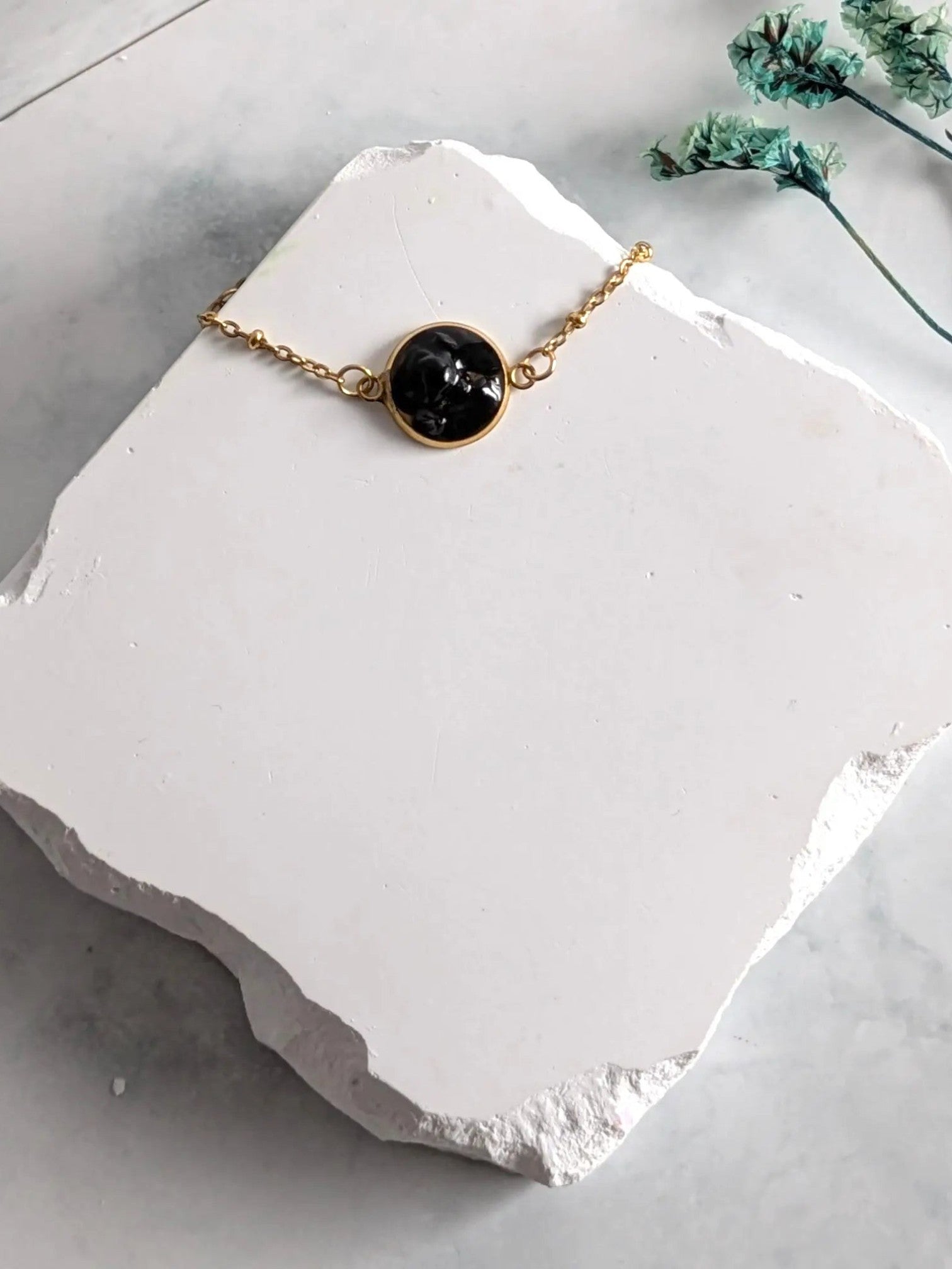 Citrinmagi armband med rund svart turmalin i 18k guldpläterad fattning på en vit stenplatta.